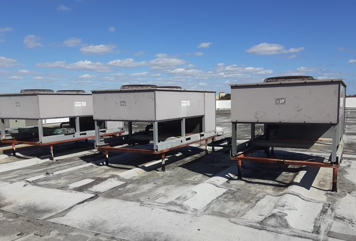 Multiple large HVAC units installed on a flat rooftop under a blue sky.